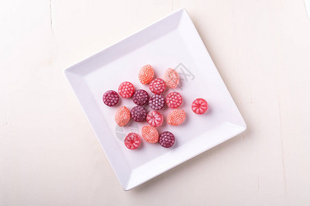 白盘上多汁浆果形式的糖果棒糖白色背景图片