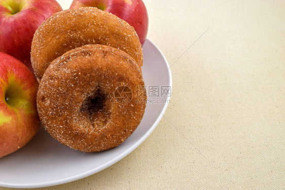 白色盘子上的新鲜苹果甜圈被红苹果包围有图片