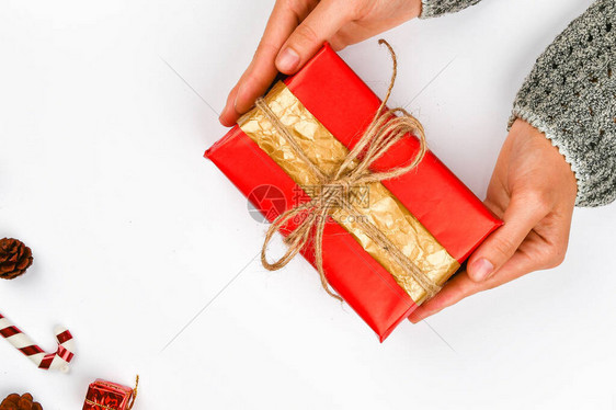手中的红色和礼品包装用白色上的蝴蝶结针织DIY礼品包装女人的手给了一个包裹的礼物圣诞礼图片