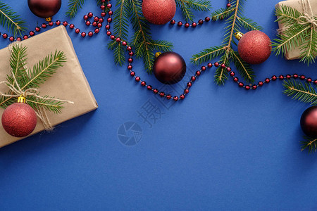 框架由圣诞装饰品圣诞树枝球蓝色背景的礼物制成明信片模板或模型平躺图片