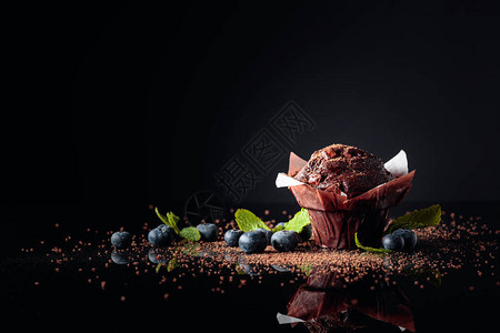 巧克力松饼洒满巧克力碎屑黑色反射背景浆果和薄荷的胡萝图片