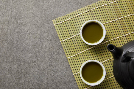 在竹桌垫上黑茶壶附近的青茶叶白图片