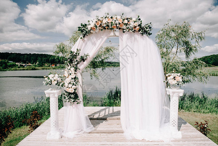 在湖边或河户外复制空间附近装饰鲜花和绿色的圆环婚礼拱门图片