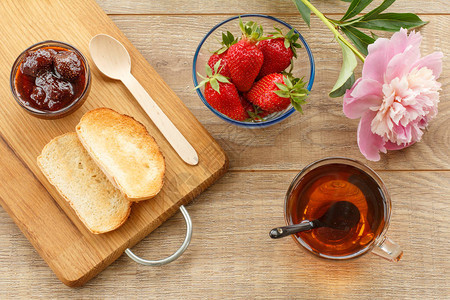 茶杯自制草莓果酱和玻璃碗里新鲜的浆果木勺切割板上的烤图片