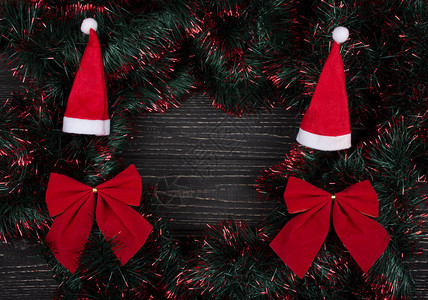 圣诞帽红色圣诞蝴蝶结和绿色和红色金属丝在黑色木质上形成框架图片