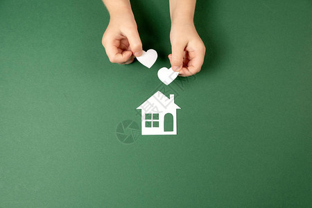 儿童手握着白纸屋和绿色背景的心脏图片