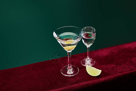 在绿色隔离的丝绒表面上的牙签上带有苦艾酒和全橄榄的小酒杯和鸡尾酒杯图片