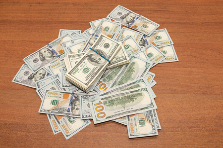 在木制桌背景布局上的几百张钞票分散在办公桌上的一捆钱财富图片