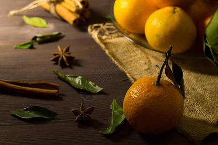 含绿叶的新鲜橙色橘子和木本底在黑桌上配有肉桂和香料的图片