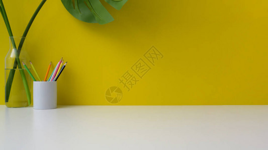 黄墙背景白桌上有复制空间铅笔和花瓶的多彩工作背景图片