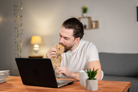 有个年轻人在家工作用电脑在桌子上吃图片