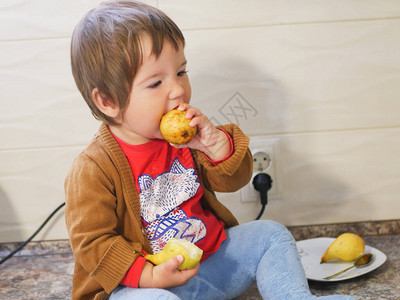 小孩在厨房里吃梨子男孩在高调的背景图片