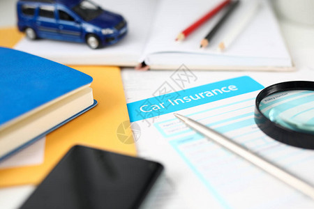 签署有关客户汽车保险的重要文件的特写镜头桌子上的车辆铅笔记本智能手机和放大镜的蓝色模图片