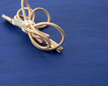 在蓝色木制背景的纺织刮线上用电设备充电的扭曲金色图片