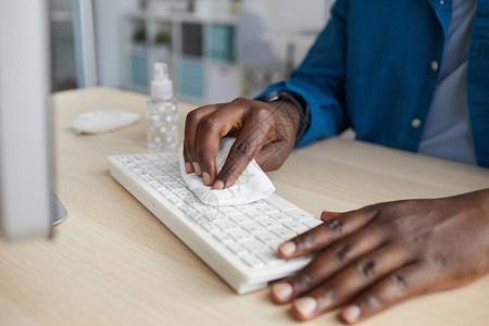 非洲裔美国青年男子在大流行后办公室办公桌工作时用消毒湿巾擦拭键盘复图片