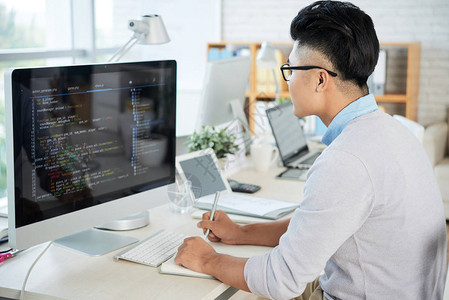 亚洲年轻人在现代办公室工作时观看计算机监视器和素描手册的侧面观点ECN4Sub22背景图片