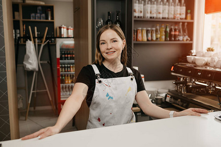 一位穿着白色围裙的女咖啡师在咖啡馆的酒吧后面摆姿势一位漂亮的女老板张开双臂图片