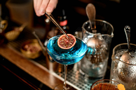 酒保手用柠檬片装饰的杯子和蓝色鸡尾酒背景图片