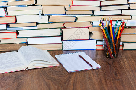 开放式教科书笔记本眼镜铅笔架木桌上的一叠旧书教育理念背景许多书堆背景图片