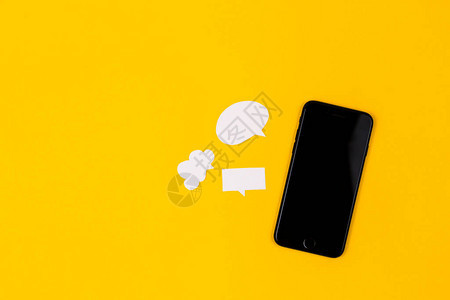 黄色背景上有纸泡的智能手机沟通理念顶视图复制空图片