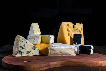 不同种类的奶酪黑色背景的木板上带有干酪红豆蓝奶酪等的白芝背景图片