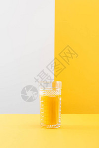 灰色和黄色背景上的一杯新鲜美味的黄色冰沙图片