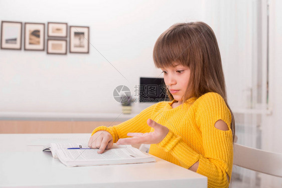 一个长头发和刘海的金发女学生坐在家里的桌子旁看书的镜头她看不懂图片