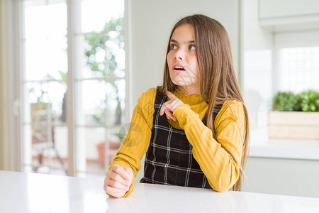 在家穿着休闲黄色毛衣的金发美女小孩用食指着一边担心和紧张图片