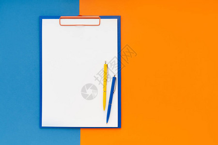 空白剪贴板模型和蓝橙色背景上的两支笔图片