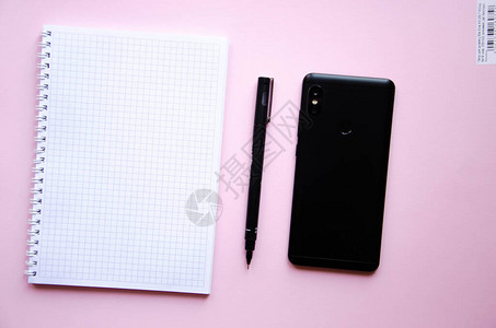 粉红色背景上的平方笔记本黑笔和记本和智能手机笔记本图片