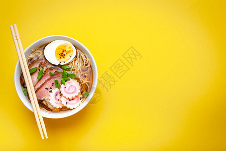 白色陶瓷碗中的美味日本面条汤拉面肉汤猪肉片火影忍者淡黄色背景的蛋黄背景图片