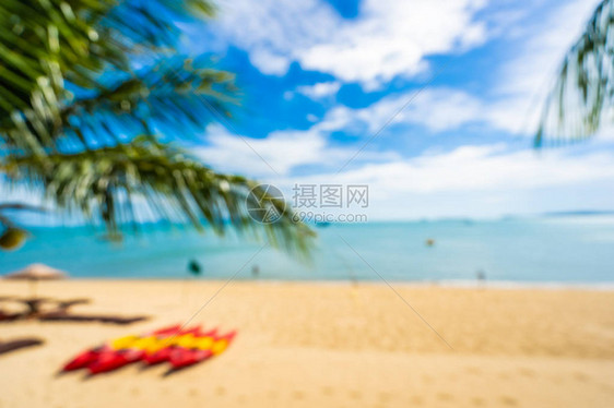 抽象的模糊和散焦美丽的热带海滩和洋与椰子棕榈树和伞椅子在蓝天和白图片
