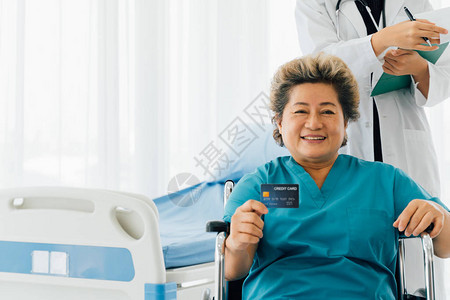 坐在轮椅和在医院病房展示信用卡时笑着微笑的身着便服的亚洲高级图片