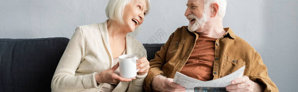 穿着茶杯的高级女子和丈夫在沙发上聊天时笑着报纸的丈图片