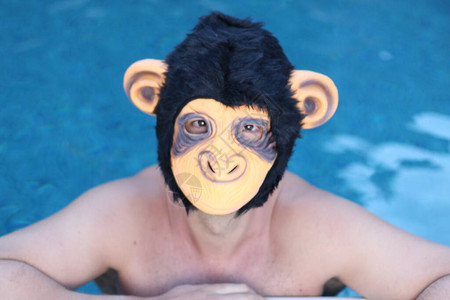在游泳池中蒙猴子面具的英俊青年图片