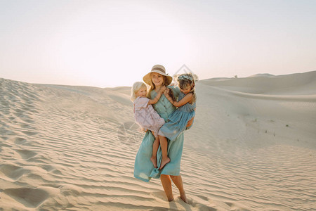 年轻美丽的母亲和两个小女孩在迪拜沙漠的沙图片
