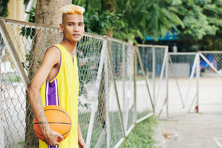 帅气的年轻瘦小球员在街头篮球场周围靠着金图片