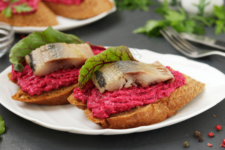 深色混凝土背景的白盘上的甜菜奶油酪和鲱鱼三明治图片