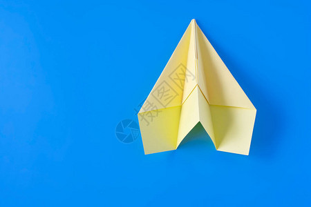 蓝色背景上的黄色纸折飞机特写图片