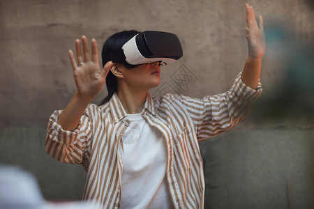 身穿VR装备并在享受未来主义室内沉浸式体验的同时做手势的亚洲图片