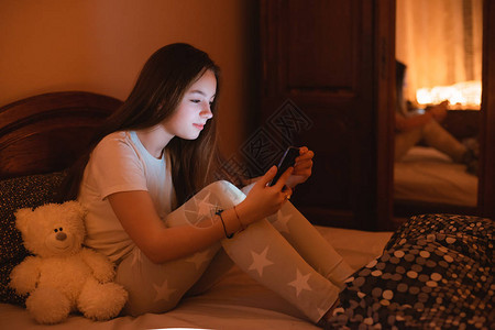 十几岁的女孩晚上躺在床上使用智能手机失眠和睡前智能手机的危害不健康的睡眠青少年对社背景图片