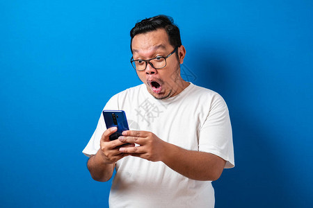 身穿白色T恤的亚洲胖子对他从智能手机收到的好消息感到惊讶男人在智能手机上滚下眼镜时背景图片