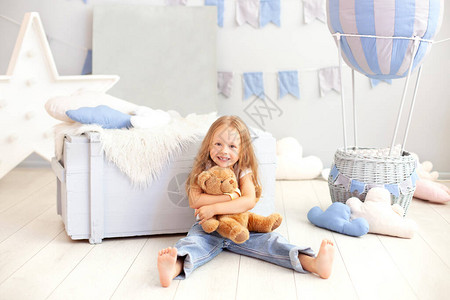 微笑的金发小女孩在装饰气球的背景上拥抱一只泰迪熊孩子在儿童房里玩具童年背景图片