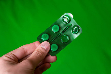 照片绿色包装药丸在绿色背景上的手中图片