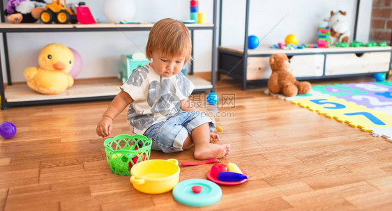 可爱的蹒跚学步的孩子坐在地板上用塑料餐具和食物在幼儿园的许多图片