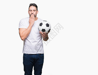 年轻人拿着足球在孤立的背景上用手捂住嘴图片
