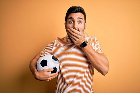 有胡子的帅哥在踢足球时拿着橄榄球在黄色背景上摇着嘴说错话图片