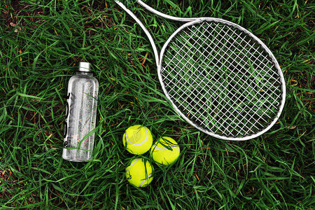 网球比赛绿草上的一瓶水球拍和网球图片