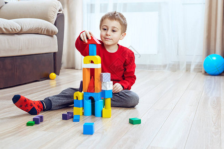 小男孩坐在木地板上玩用五颜六色的木块建造构塔舒图片