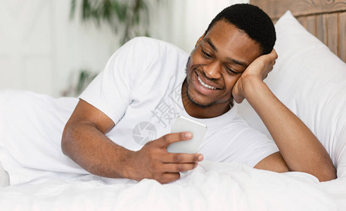 周末早晨在家睡觉时使用智能电话聊天的黑人男子图片